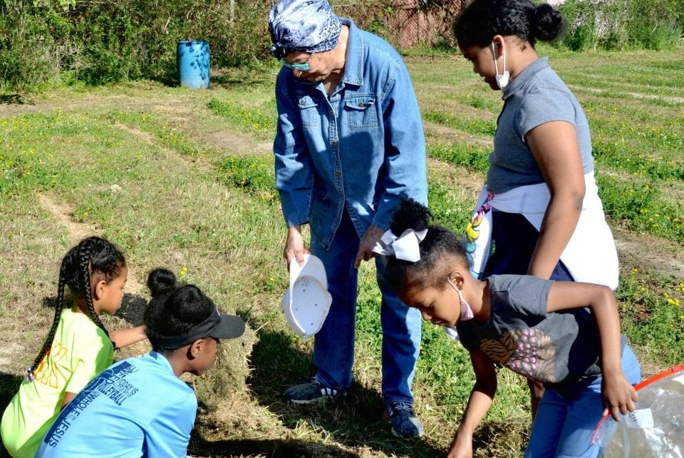 Neighborhood children gather around Eva Iford Friday as they examine the soil for the First Harvest Community Garden project.
